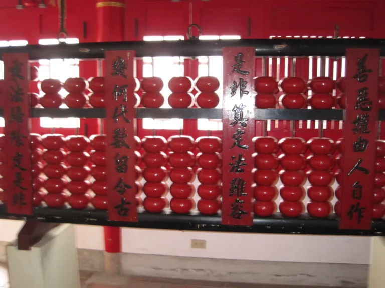A large wooden abacus with rows of red beads hanging across a temple hall, its frame carved with a couplet about weighing good and evil.