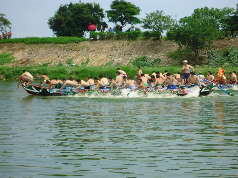 Two narrow wooden dragon boats, paddled by village crews, racing side by side along the narrow Erlong river between grassy banks in Jiaoxi, Yilan.